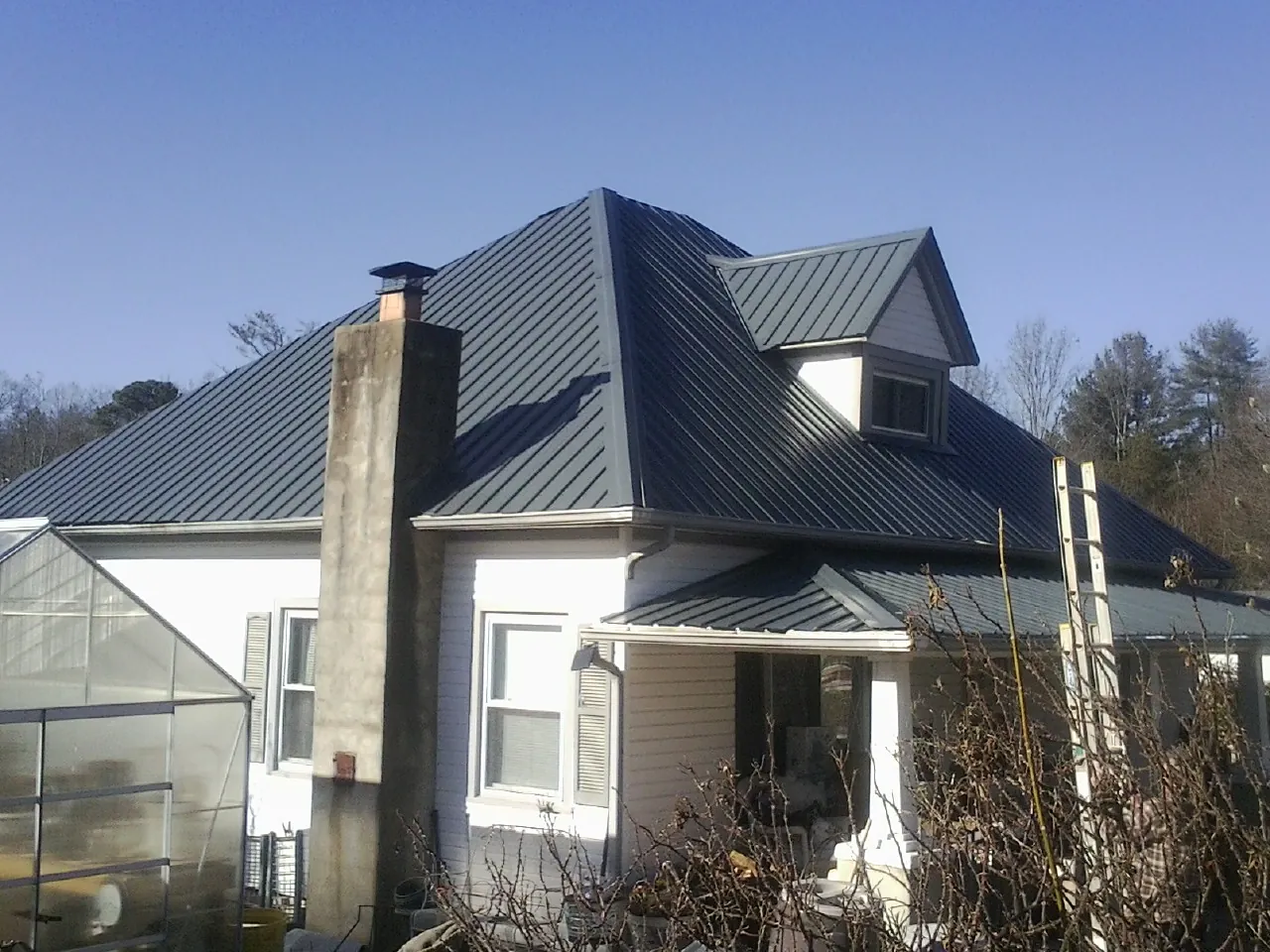 Dark blue standing seam metal roof on a white farmhouse with dormer in Rockfall