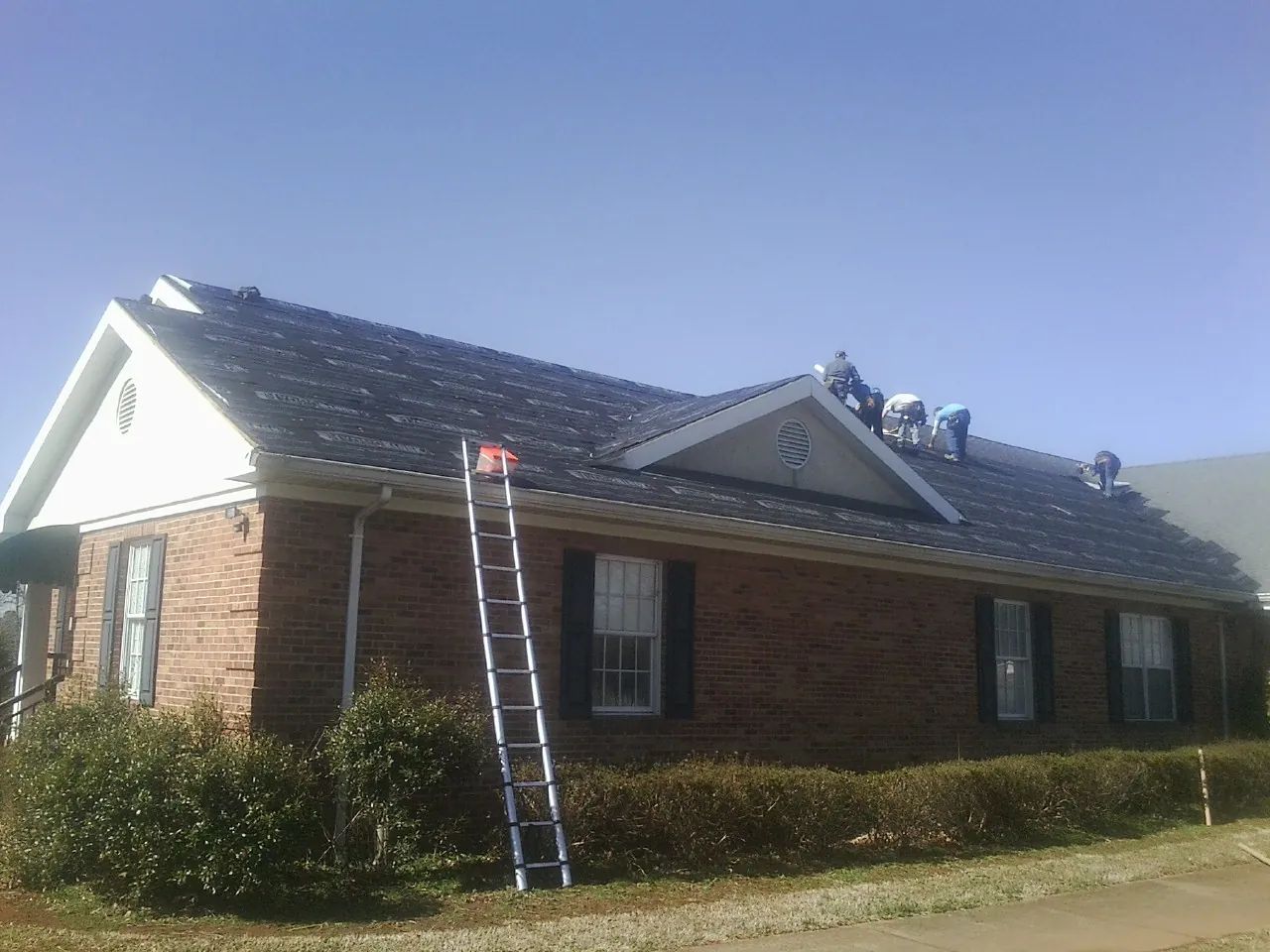 Crew tearing shingles off a brick ranch roof with a ladder set — Metal Roof Repair work by our crew in Rockfall