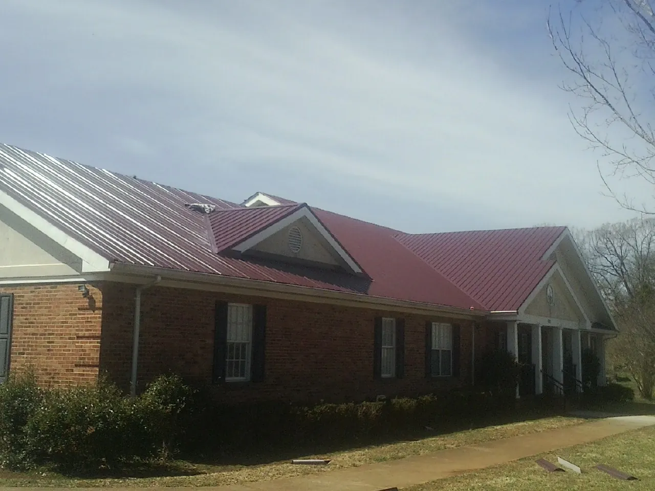 Red metal roof with gabled entries on a long brick building, from a Hail Damage Roof Repair job in Rockfall