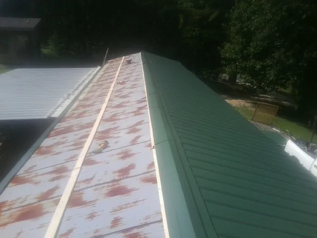Old rusted panels beside newly installed green metal roofing — Wind Damage Roof Repair by Roofing Brothers in Rockfall