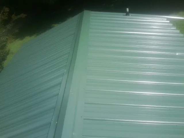 New green metal panels meeting at the ridge of a roof — Flat Roof Repair work by our crew in Rockfall