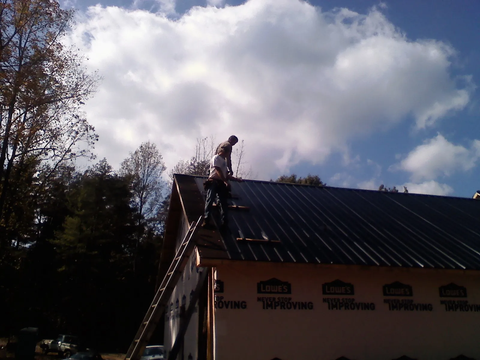 Roofer fastening dark metal panels high against a cloudy sky, from a Roof Inspection job in Rockfall